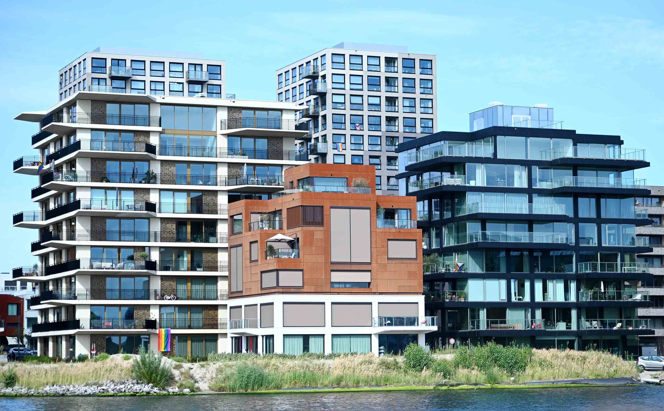 Een betonnen en stalen draagconstructie in aanbouw tegen een blauwe lucht, met vloerplaten, kolommen en randbeveiliging zichtbaar per verdieping, en een torenkraan ernaast.