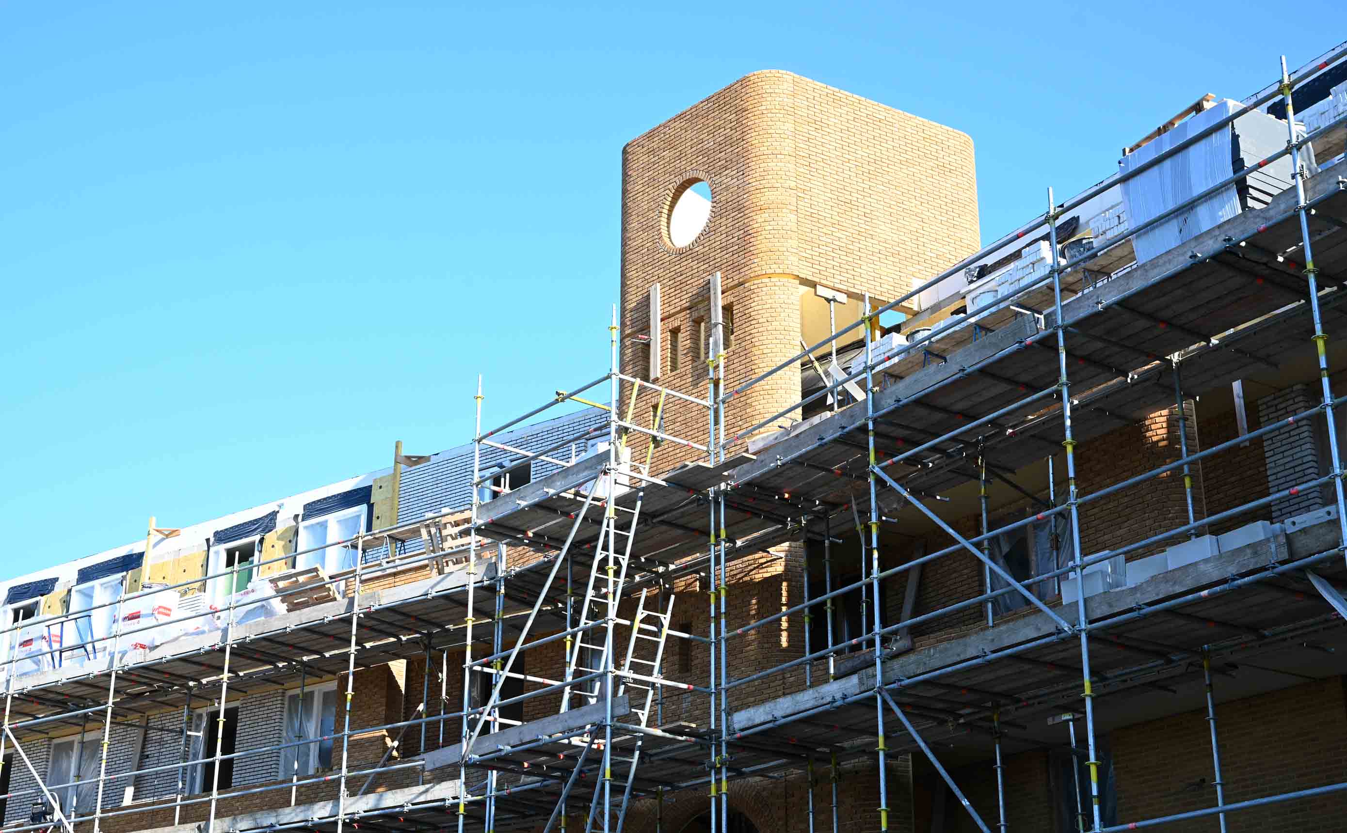 Scaffolding around a brick facade under construction, with insulation panels fitted between window openings.