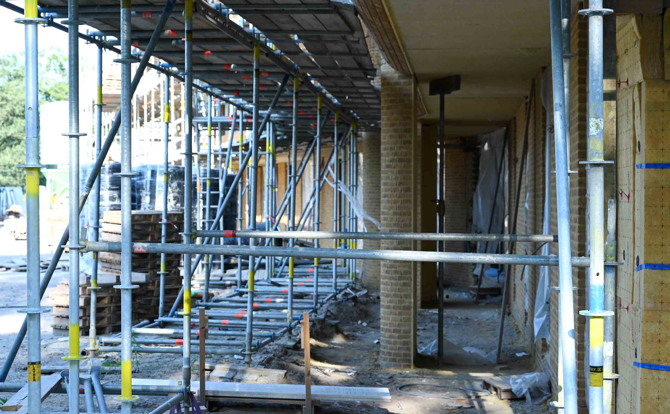 Het interieur van een woongebouw dat nog in aanbouw is, gezien door de steiger, met kaal metselwerk, een deuropening en bouwfolie.