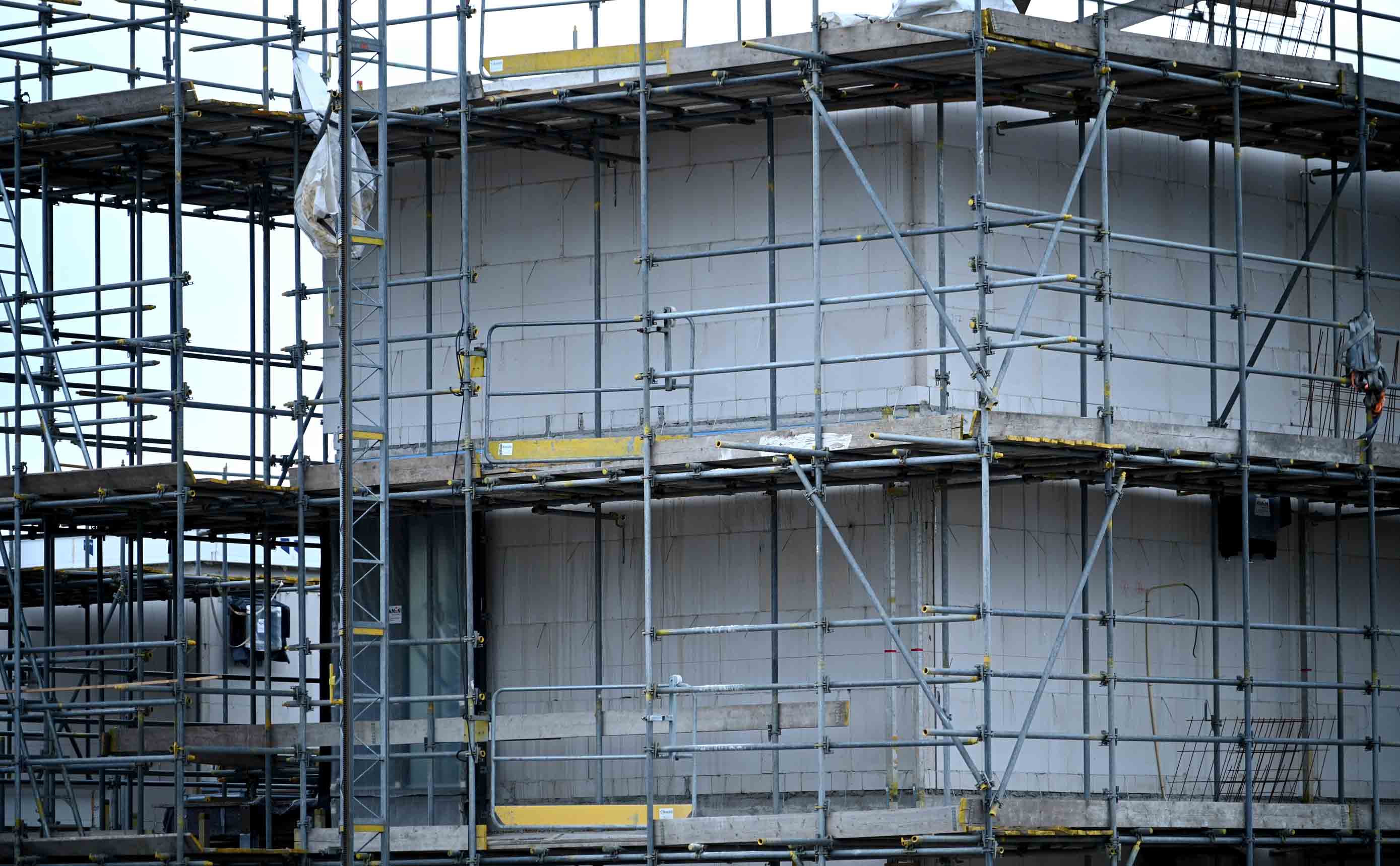 A concrete facade behind scaffolding on a building under construction, floor edges and elements exposed.