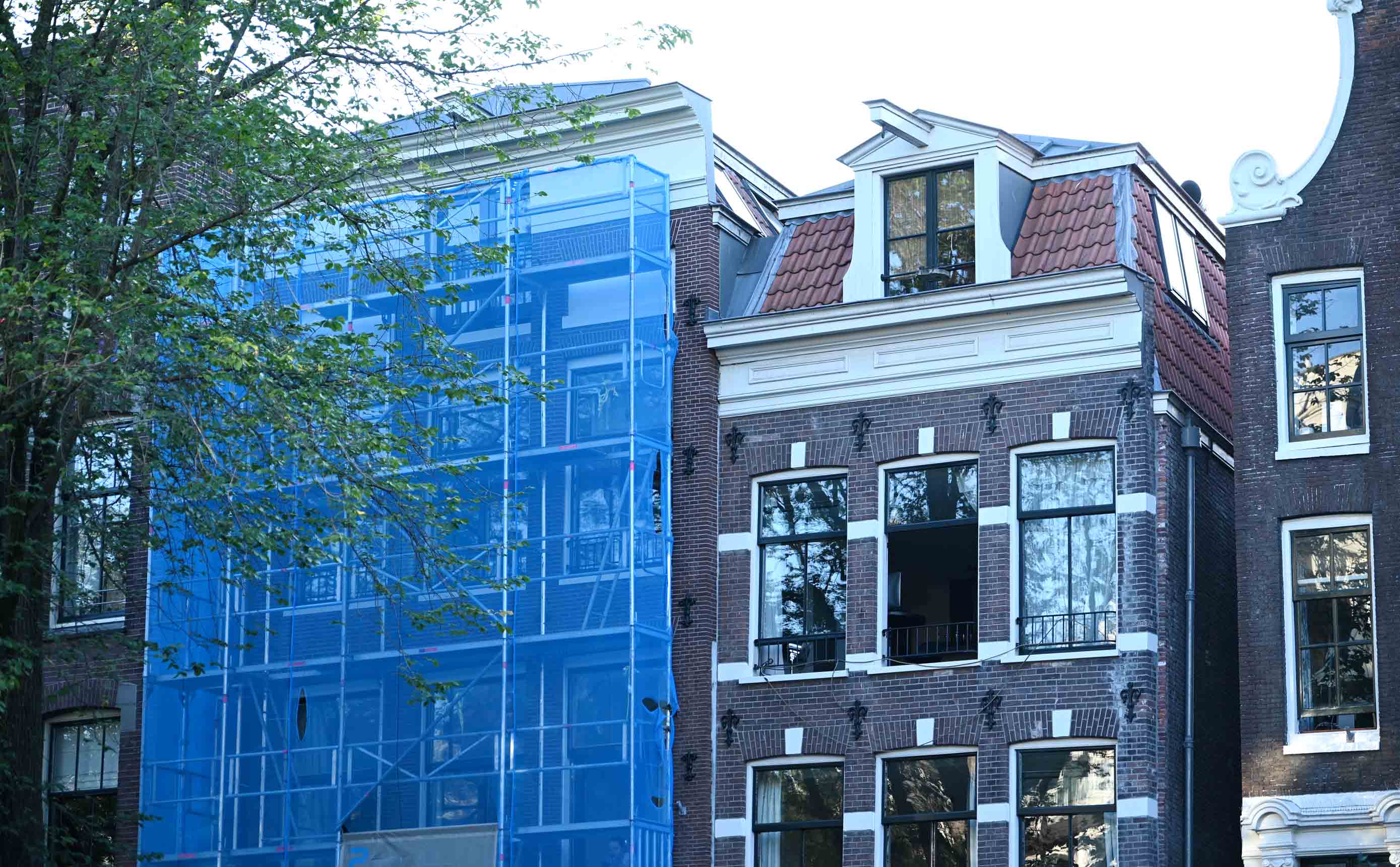 Een woongebouw in aanbouw in de steigers, kale betonvloeren en wanden van kalkzandsteen zichtbaar per verdieping, met een werkman op de bovenste laag.