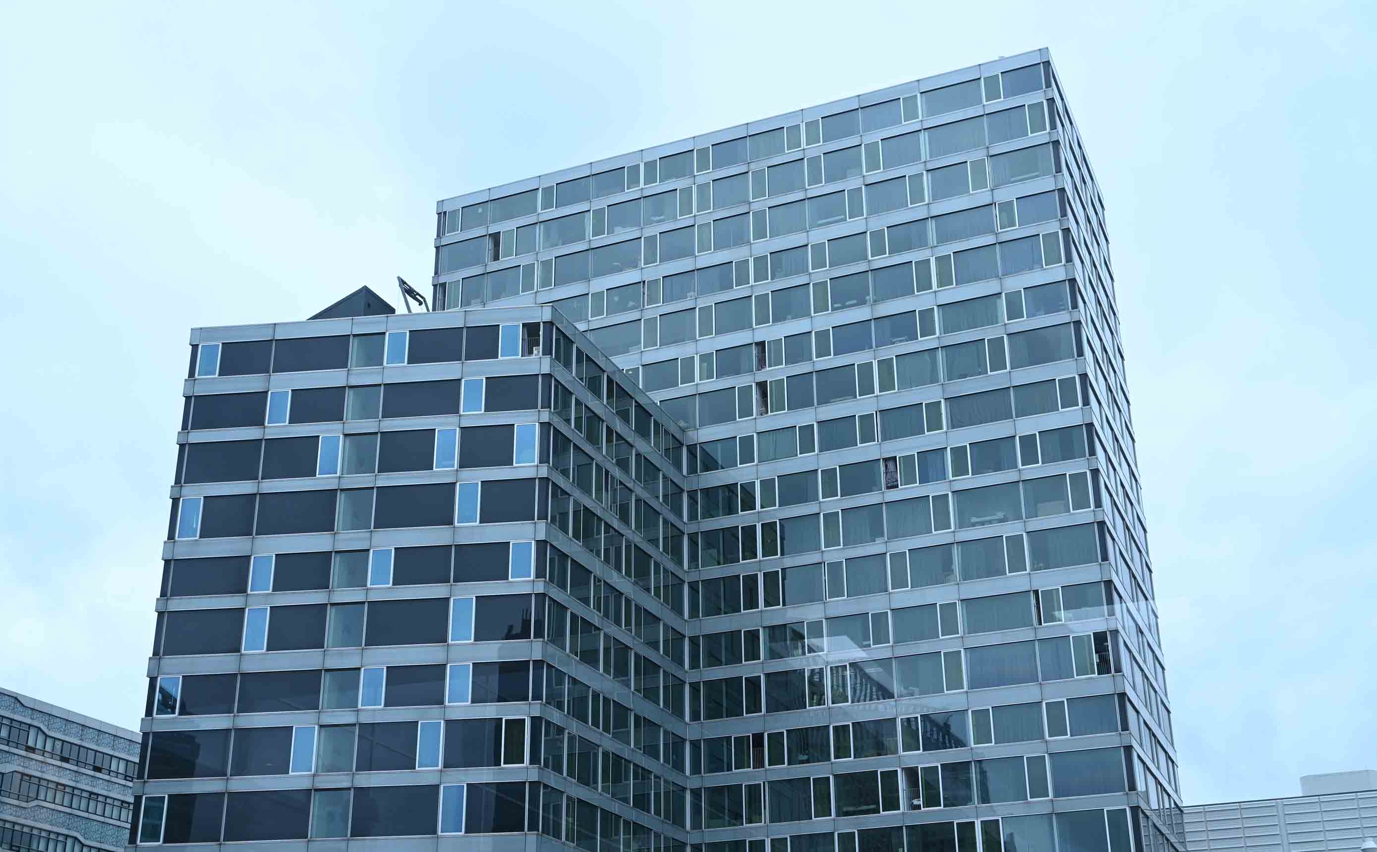 A modern glass office tower photographed from below, with a strict grid of curtain-wall panels and windows, each floor and bay clearly repeated against a pale sky.